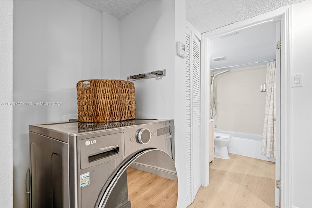 laundry room with light wood-type flooring, a textured ceiling, and washer / clothes dryer