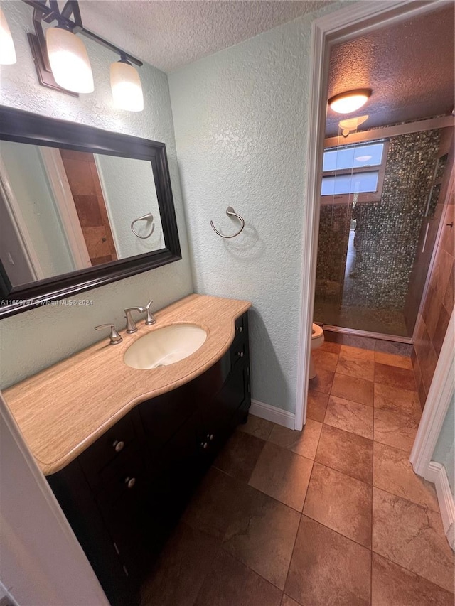 bathroom with vanity, a textured ceiling, a tile shower, toilet, and tile patterned floors