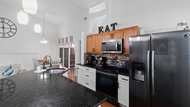 kitchen with dark stone counters, stainless steel appliances, sink, white cabinetry, and hanging light fixtures