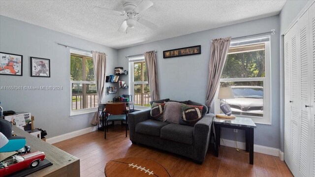 living area with a healthy amount of sunlight, a textured ceiling, ceiling fan, and dark wood-type flooring