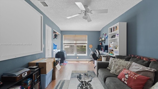 living room featuring ceiling fan, light wood-type flooring, and a textured ceiling