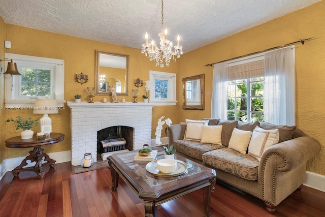 living room featuring dark wood-type flooring, a textured ceiling, a brick fireplace, and a chandelier