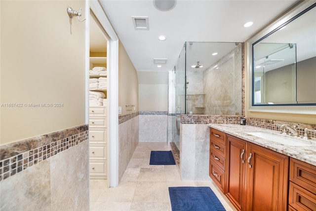 bathroom featuring tile patterned flooring, a shower with door, tile walls, ceiling fan, and vanity