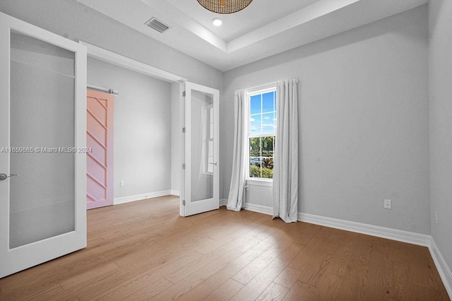 unfurnished room with french doors, light wood-type flooring, and a raised ceiling