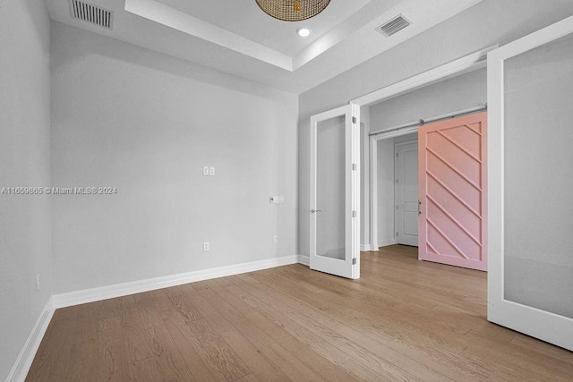 unfurnished bedroom featuring a raised ceiling, a barn door, light hardwood / wood-style flooring, and french doors