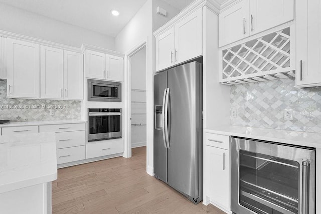 kitchen featuring beverage cooler, stainless steel appliances, light hardwood / wood-style flooring, backsplash, and white cabinets