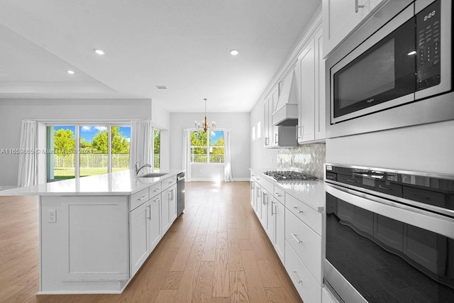 kitchen with sink, stainless steel appliances, tasteful backsplash, a kitchen island with sink, and white cabinets