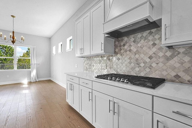 kitchen with stainless steel gas cooktop, an inviting chandelier, backsplash, white cabinets, and custom exhaust hood