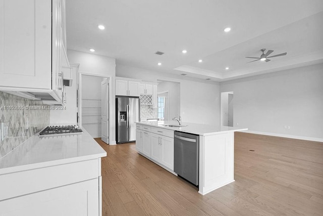 kitchen with a center island with sink, white cabinets, sink, light wood-type flooring, and stainless steel appliances