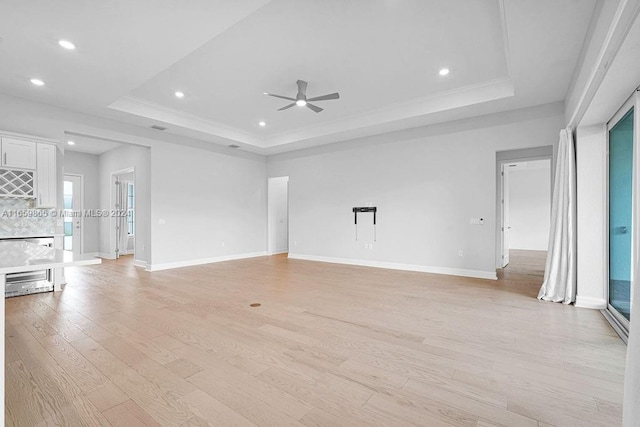 unfurnished living room with a tray ceiling, ceiling fan, and light hardwood / wood-style floors