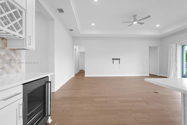 unfurnished living room with light wood-type flooring, a tray ceiling, wine cooler, and ceiling fan