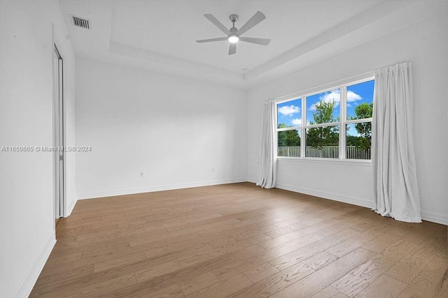 spare room featuring a tray ceiling, ceiling fan, and light wood-type flooring