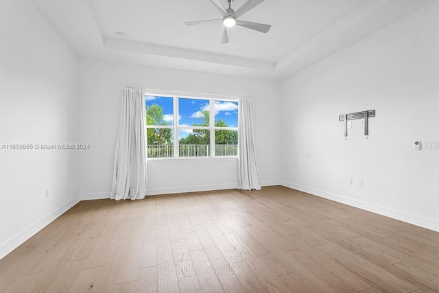 unfurnished room with ceiling fan, a raised ceiling, and light wood-type flooring