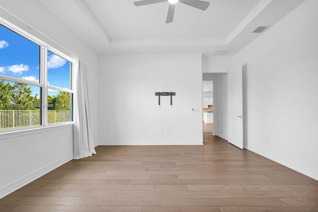 unfurnished room featuring ceiling fan, light wood-type flooring, and a tray ceiling