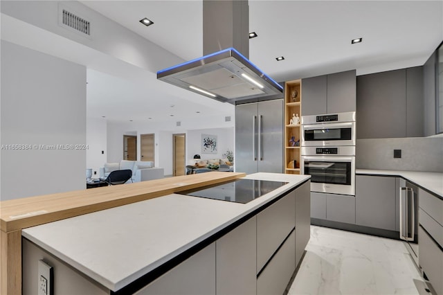 kitchen featuring island exhaust hood, appliances with stainless steel finishes, a center island, and gray cabinetry