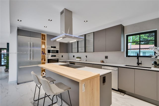 kitchen featuring sink, island exhaust hood, gray cabinets, stainless steel appliances, and a kitchen bar