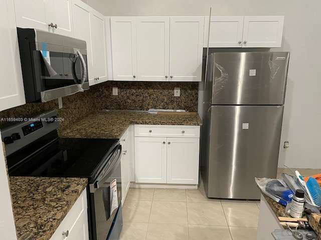 kitchen featuring appliances with stainless steel finishes, white cabinetry, light tile patterned floors, and dark stone counters