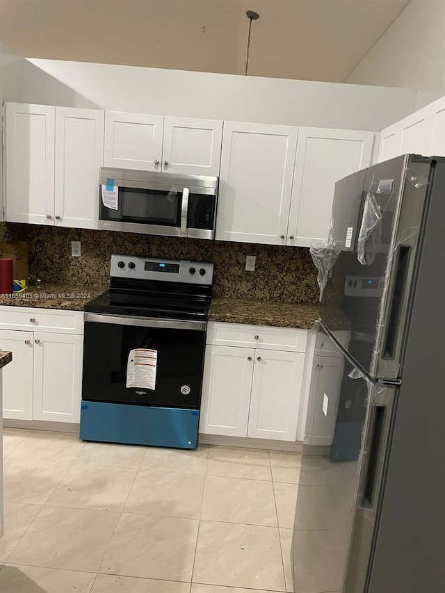 kitchen with light tile patterned floors, appliances with stainless steel finishes, white cabinetry, dark stone counters, and tasteful backsplash