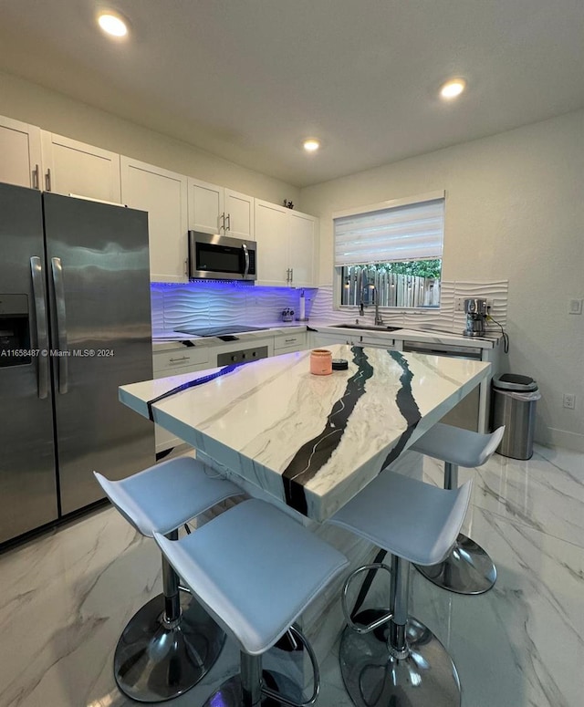 kitchen with a center island, stainless steel appliances, decorative backsplash, light stone counters, and white cabinets