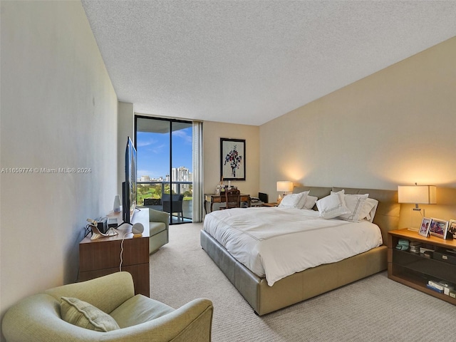 bedroom with a textured ceiling, light colored carpet, and a wall of windows