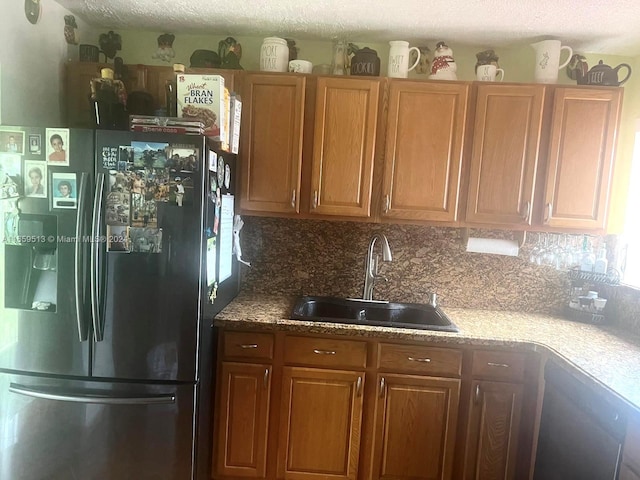 kitchen with a textured ceiling, sink, stainless steel fridge, and decorative backsplash