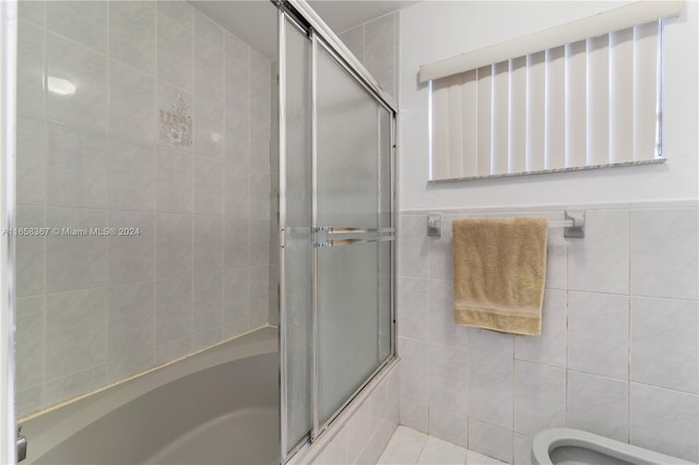 bathroom with tile walls, toilet, and bath / shower combo with glass door