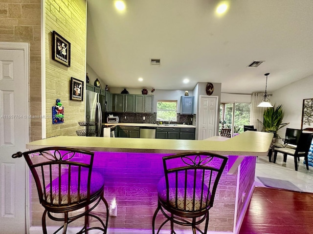 kitchen featuring decorative light fixtures, kitchen peninsula, stainless steel appliances, gray cabinets, and hardwood / wood-style flooring