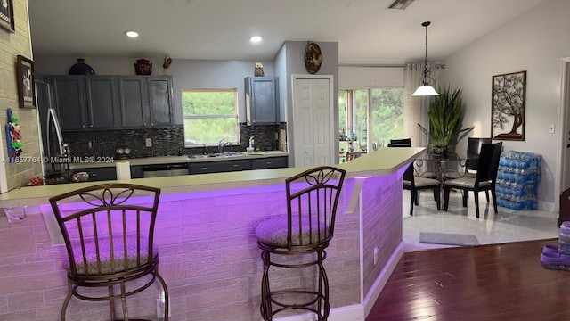 kitchen with tasteful backsplash, decorative light fixtures, sink, dark wood-type flooring, and a breakfast bar area