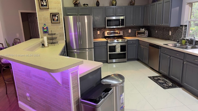 kitchen with light tile patterned floors, appliances with stainless steel finishes, a breakfast bar, sink, and gray cabinets