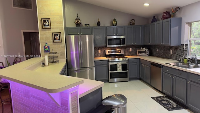 kitchen with light tile patterned floors, a kitchen breakfast bar, kitchen peninsula, sink, and appliances with stainless steel finishes