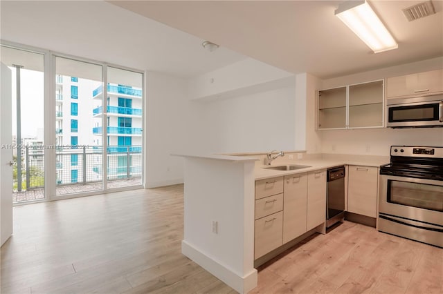 kitchen with appliances with stainless steel finishes, kitchen peninsula, sink, and light hardwood / wood-style flooring