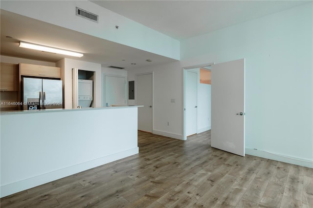 kitchen with electric panel, stacked washer / dryer, light hardwood / wood-style floors, and stainless steel fridge with ice dispenser