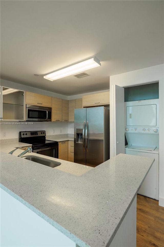 kitchen featuring light stone counters, stacked washer / dryer, light brown cabinets, appliances with stainless steel finishes, and dark hardwood / wood-style flooring