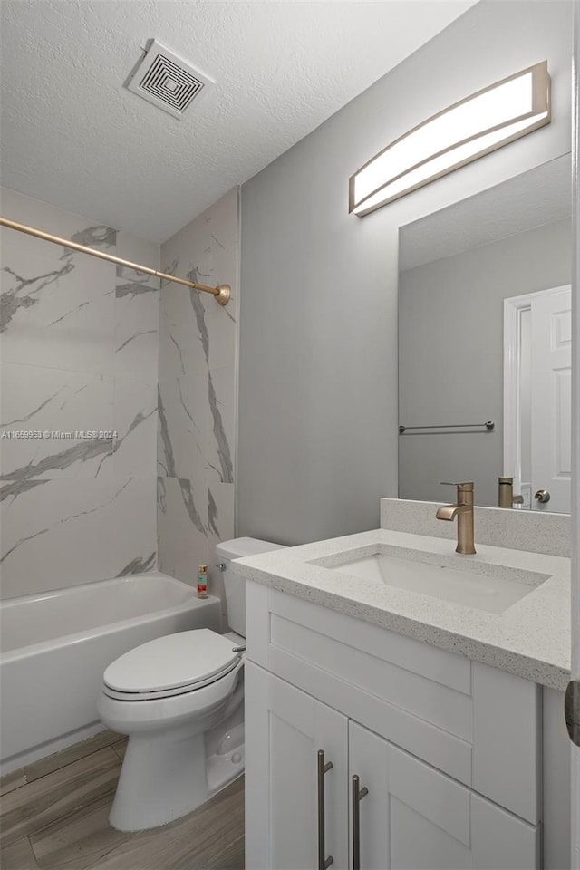 full bathroom with vanity, a textured ceiling, tiled shower / bath combo, toilet, and hardwood / wood-style floors