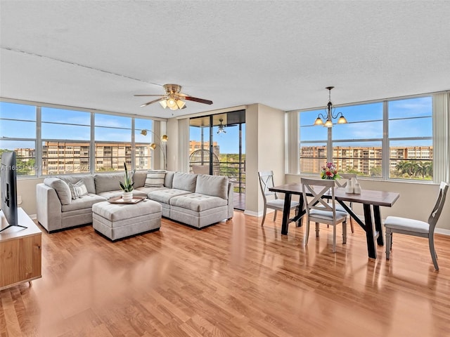 living room featuring ceiling fan with notable chandelier, light hardwood / wood-style floors, and a textured ceiling