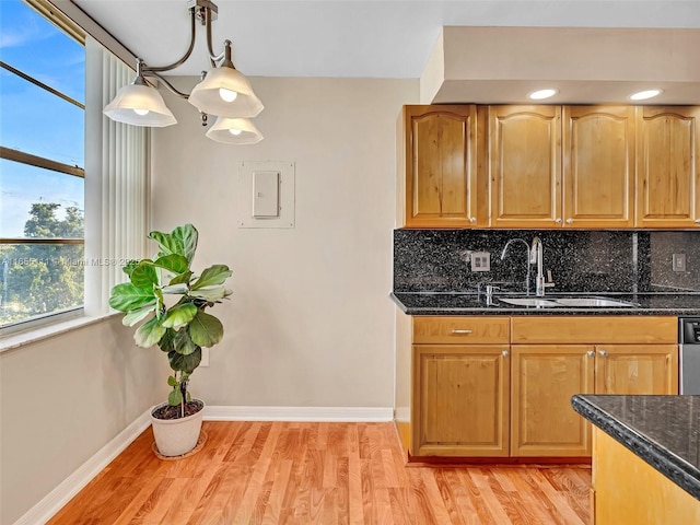 kitchen featuring sink, dark stone countertops, hanging light fixtures, backsplash, and light hardwood / wood-style floors