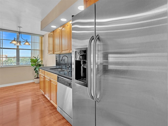 kitchen featuring appliances with stainless steel finishes, pendant lighting, tasteful backsplash, sink, and a chandelier