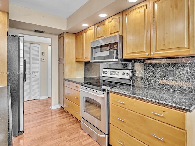 kitchen with appliances with stainless steel finishes, dark stone countertops, backsplash, and light hardwood / wood-style floors