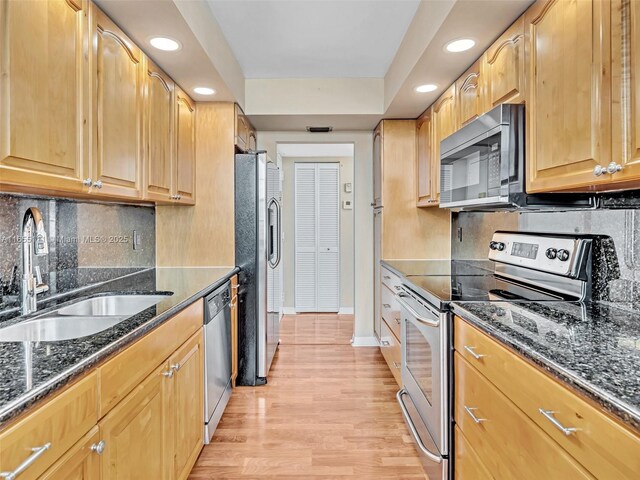 kitchen featuring sink, dark stone countertops, stainless steel appliances, tasteful backsplash, and light hardwood / wood-style floors