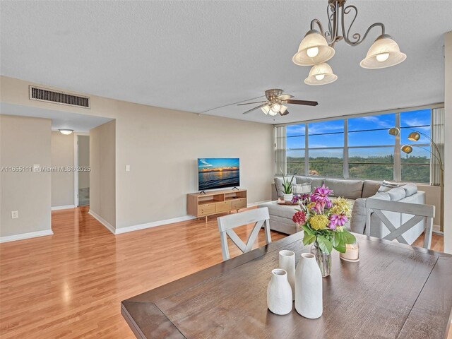 dining space with ceiling fan with notable chandelier, hardwood / wood-style floors, and a textured ceiling