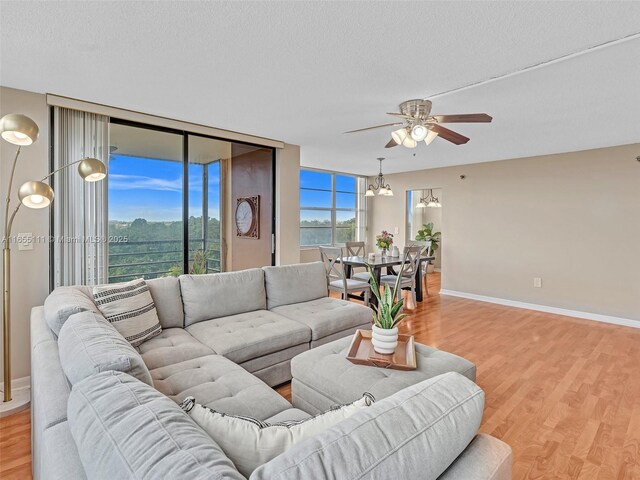 living room with ceiling fan with notable chandelier, a textured ceiling, and light hardwood / wood-style floors