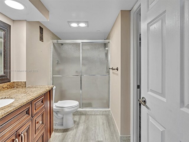 bathroom featuring wood-type flooring, toilet, a shower with shower door, and vanity