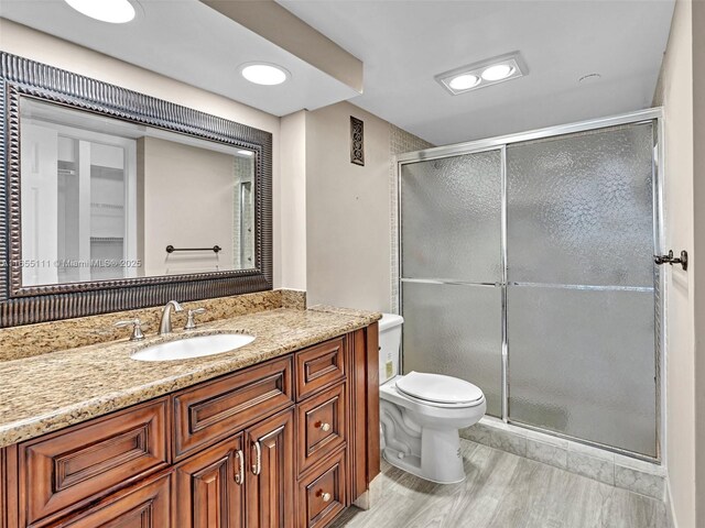 bathroom featuring vanity, wood-type flooring, a shower with shower door, and toilet