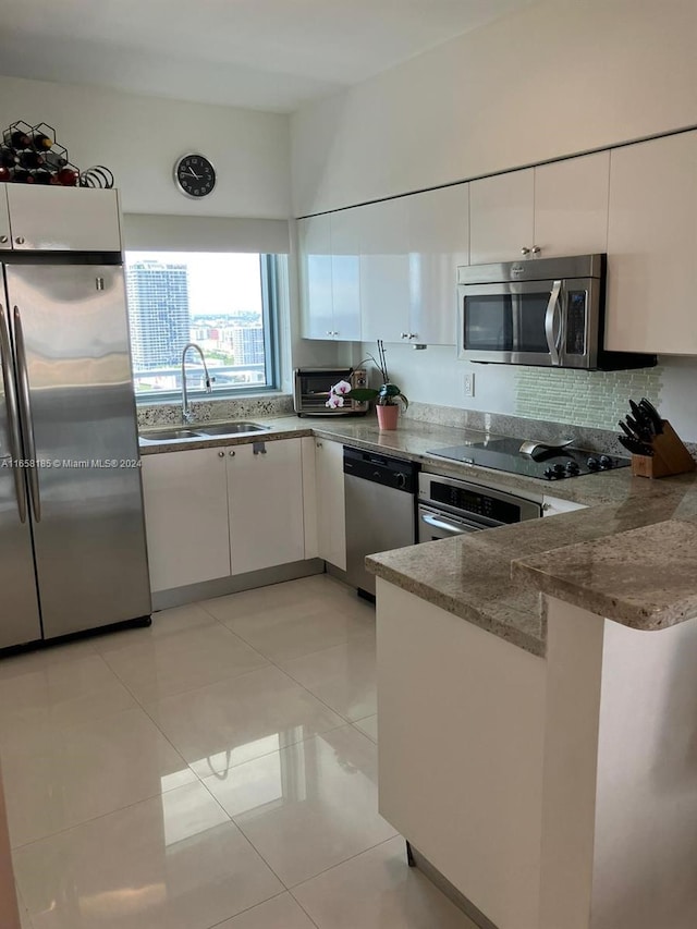 kitchen with white cabinets, light tile patterned floors, kitchen peninsula, backsplash, and stainless steel appliances