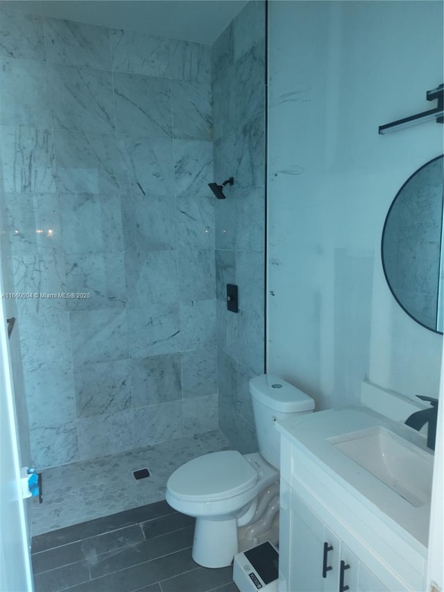 bathroom with vanity, toilet, and a tile shower