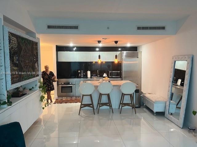 kitchen featuring white cabinetry, backsplash, decorative light fixtures, a breakfast bar, and appliances with stainless steel finishes