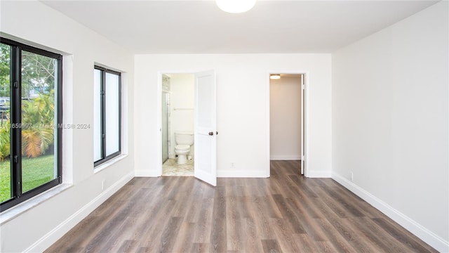 unfurnished bedroom with multiple windows, a walk in closet, dark hardwood / wood-style floors, and connected bathroom