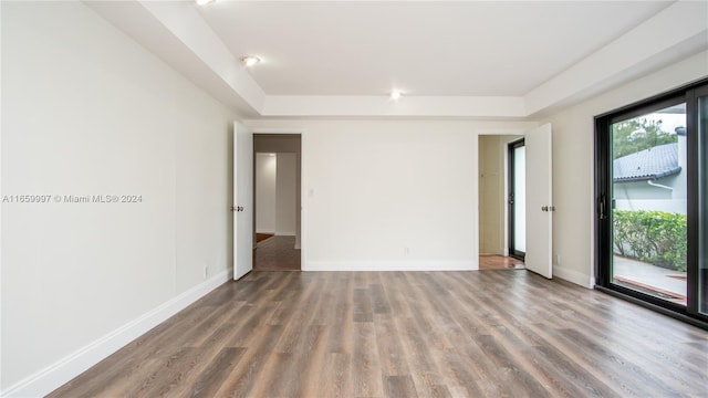 spare room with a tray ceiling, baseboards, and wood finished floors