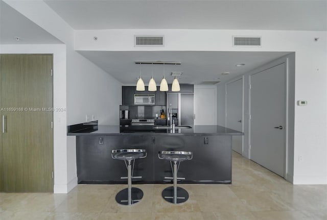 kitchen featuring appliances with stainless steel finishes, backsplash, a kitchen bar, hanging light fixtures, and kitchen peninsula