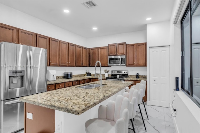 kitchen with a kitchen breakfast bar, light stone countertops, a kitchen island with sink, stainless steel appliances, and sink